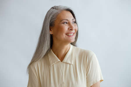Joyful lmiddle aged lady wearing beige blouse stands on light backgroundの写真素材