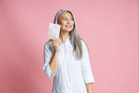 Pretty silver haired Asian woman holds gift card having ideas in studioの写真素材