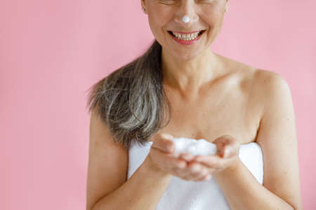 Happy middle aged lady with towel and hoary ponytail shows handful of foam in studio