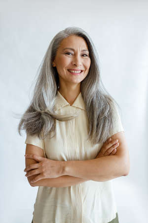 Portrait of Asian female model with long grey hair and crossed arms on light backgroundの写真素材