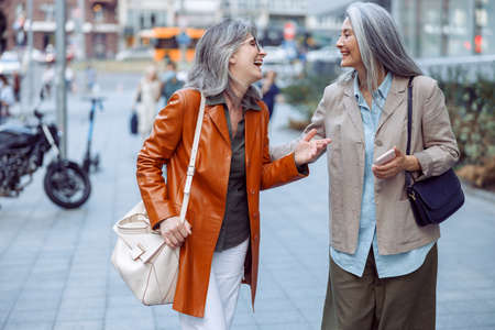 Positive senior women friends talk walking along modern city streetの写真素材