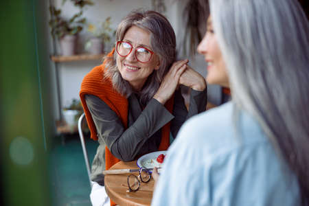 Positive mature woman with friend look through window sittin in cozy cafeの写真素材