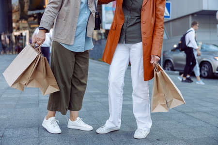 Pair of senior ladies holds shopping bags standing on modern city streetの写真素材