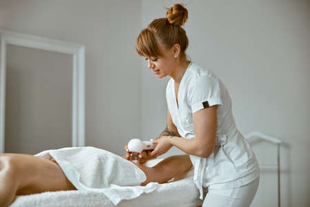 Confident female specialist is doing anticellulite leg massage to beautiful healthy caucasian female clientの写真素材