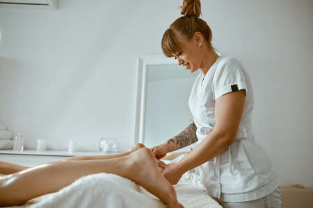Professional caucasian specialist is doing leg message at modern minimalistic salonの写真素材