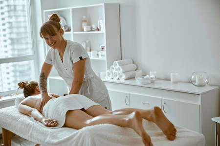 confident female specialist is doing relaxing body massage for beautyful slim caucasian lady at minimalistic spa salonの写真素材