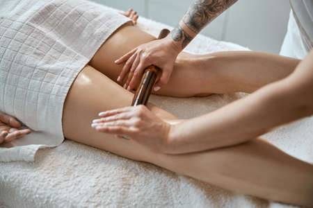 Conident female specialist is doing leg massage with bamboo stick to beautiful caucasean woman clientの写真素材