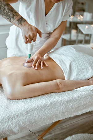professional female specialist is doing cupping therapy on the back of beautiful caucasian ladyの写真素材