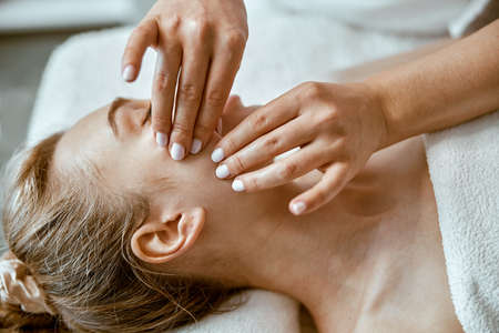 Therapist is doing face relaxing massage to a young woman in modern wellness cabinetの写真素材