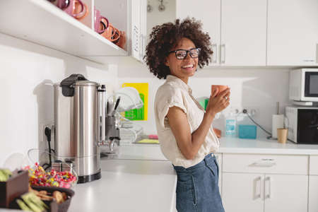 Smiling businesswoman in glasses standing with hot drink in handsの写真素材