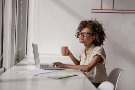 Smiling woman working with laptop and holdng coffee in handの写真素材