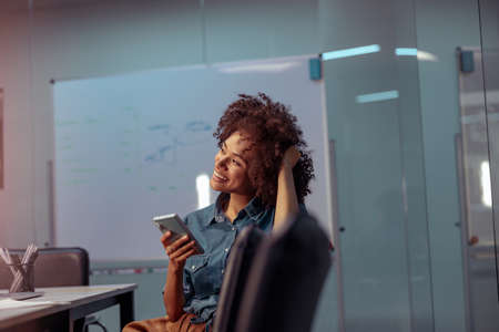 Smiling young lady using mobile phone in the officeの写真素材