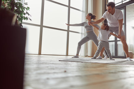 Happy parents doing yoga with daughter at homeの写真素材