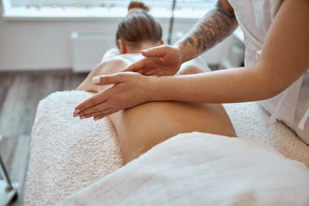 Professional confident massage master is doing procedures to caucasian woman in minimalistic modern cabinetの写真素材