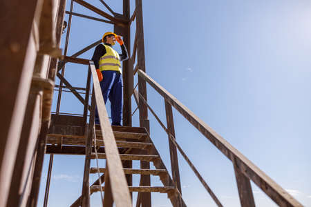 Male worker standing on top of stairs under blue sky