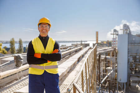 Cheerful male worker standing at industrial site against blue sky