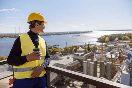 Smiling male worker with coffee cup standing outdoors at factory