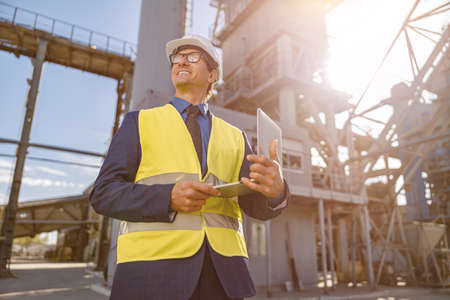 Joyful man with notebook standing outdoors at factory