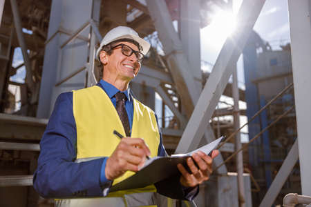 Cheerful male engineer writing documents outdoors at factoryの写真素材