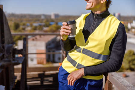 Smiling man factory worker drinking coffee outdoorsの写真素材