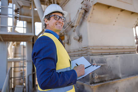 Cheerful male engine with documents working at factory