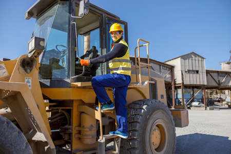 Cheerful male engineer standing on tractor stairs outdoors