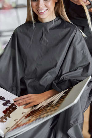 Blonde female client is chosing colour in book while hairdresser is choping her hairの写真素材