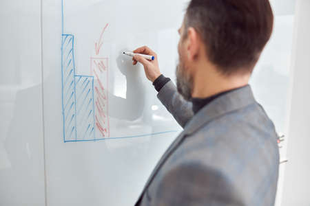 Caucasian adult man in office is writing on the glass deskの写真素材