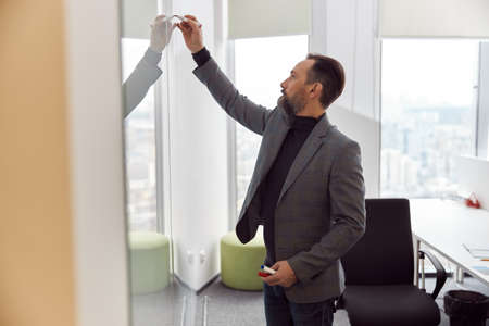 Caucasian adult man in office is writing on the glass deskの写真素材