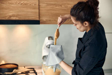 beautiful caucasian lady cook is making eclairs with help of pastry casing at homeの写真素材