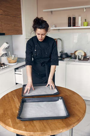 young beautiful mixed race woman spreads pastry paper on a dish in light modern kitchenの写真素材