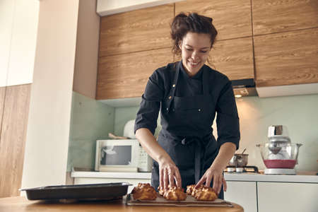 Professional confident woman is preparing custard cakes at light modern kitchen at homeの写真素材
