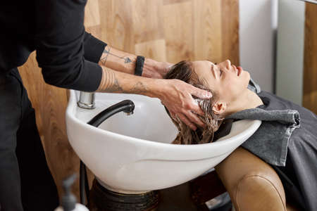 Confident stylist is washing hair of a beautiful caucasian female client at salonの写真素材