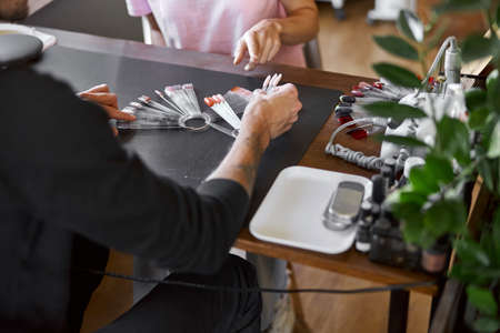 Male confident manicure master in salon with beautiful female light hair woman clientの写真素材
