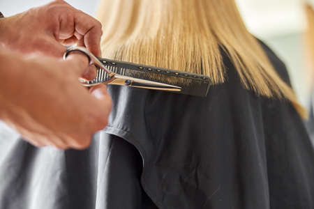 Hairdresser is choping hair of blonde woman is salon