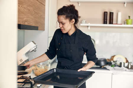young beautiful mixed race woman is preparing dough for cakes in food processorの写真素材