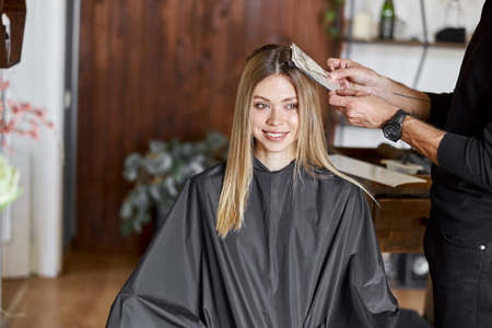 Confident male stylist is dyeing hair of blond caucasian female clientの写真素材