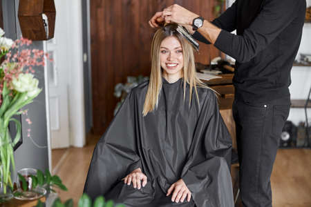 Confident male stylist is dyeing hair of blond caucasian female clientの写真素材