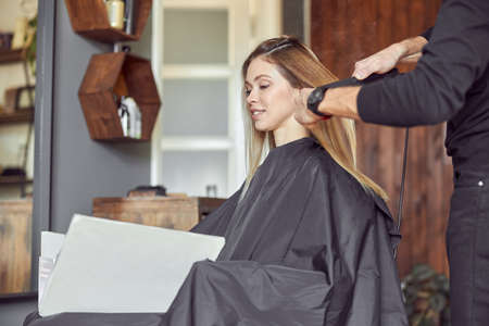 Pofessional hairdresser is combing a hair of beautiful caucasian blonde woman in modern salonの写真素材