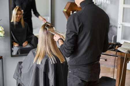 Confident male stylist is dyeing hair of blond caucasian female clientの写真素材