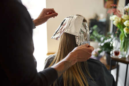 Confident male stylist is dyeing hair of blond caucasian female clientの写真素材