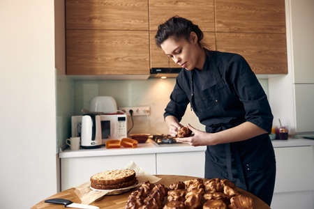 young professional female cook is preparing tasty cake at her light modern kitchenの写真素材
