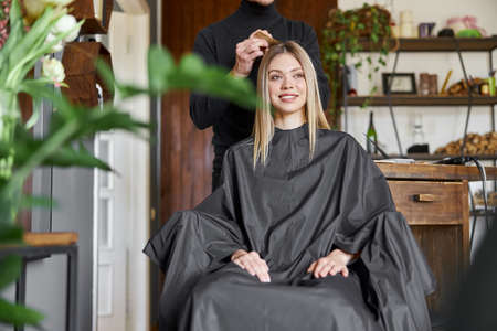 Confident male stylist is dyeing hair of blond caucasian female clientの写真素材