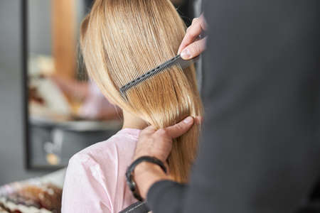 Pofessional hairdresser is combing a hair of beautiful caucasian blonde woman in modern salonの写真素材