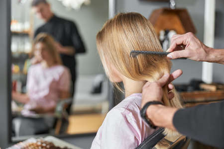 Pofessional hairdresser is combing a hair of beautiful caucasian blonde woman in modern salon