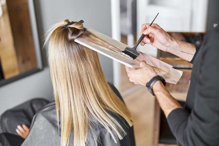 Confident male stylist is dyeing hair of blond caucasian female clientの写真素材