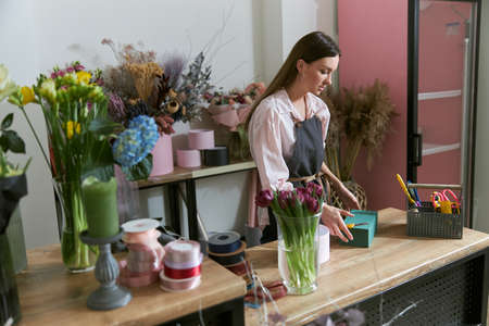 Professional florist young woman is doing bouquets at flower shopの写真素材