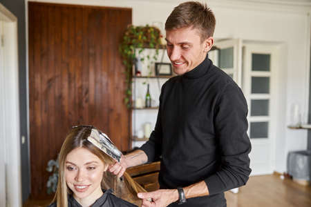 Confident male stylist is dyeing hair of blond caucasian female clientの写真素材