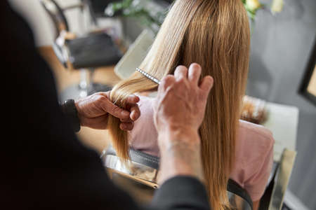 Pofessional hairdresser is combing a hair of beautiful caucasian blonde woman in modern salonの写真素材