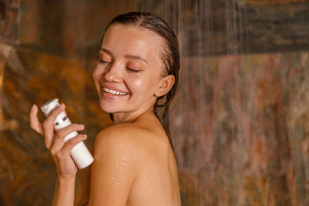 Portrait of lovely young woman standing in marble shower and washing her body using organic natural body care cosmeticsの写真素材